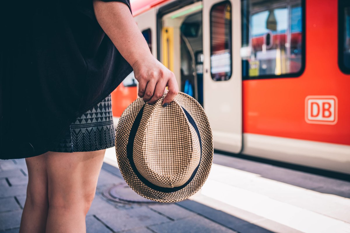 Eine Person mit einem Hut in der Hand steht am Bahnsteig